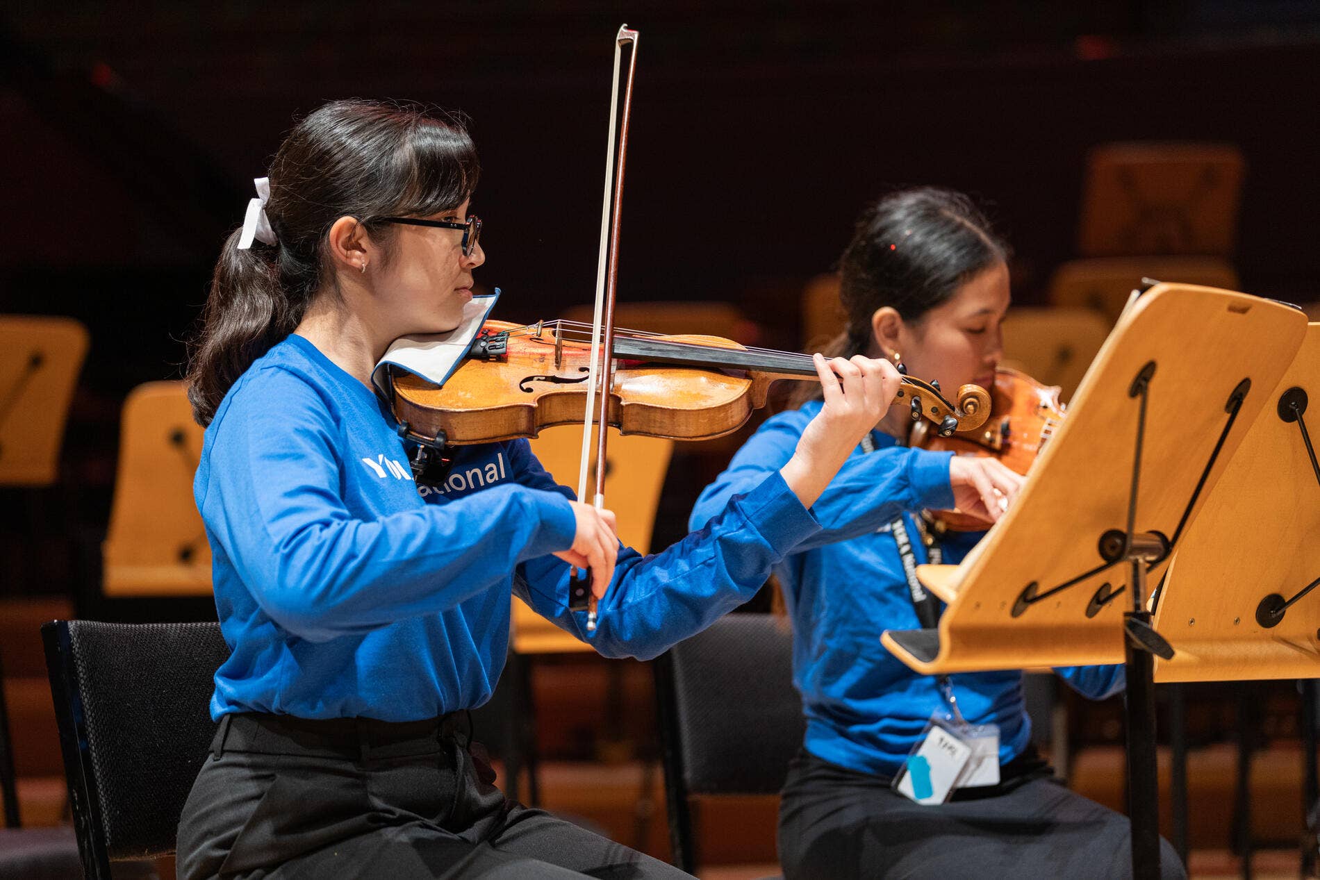 Elodie plays violin holding a bow, wearing in a blue shirt.