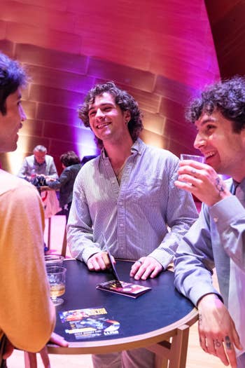 People mingle at a banquet bar, pouring drinks at a table with sparkling bottles under colorful stage lights.