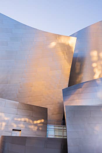 Sunlit modern building facade with curved tiled stone walls forming intersecting volumes against a blue sky