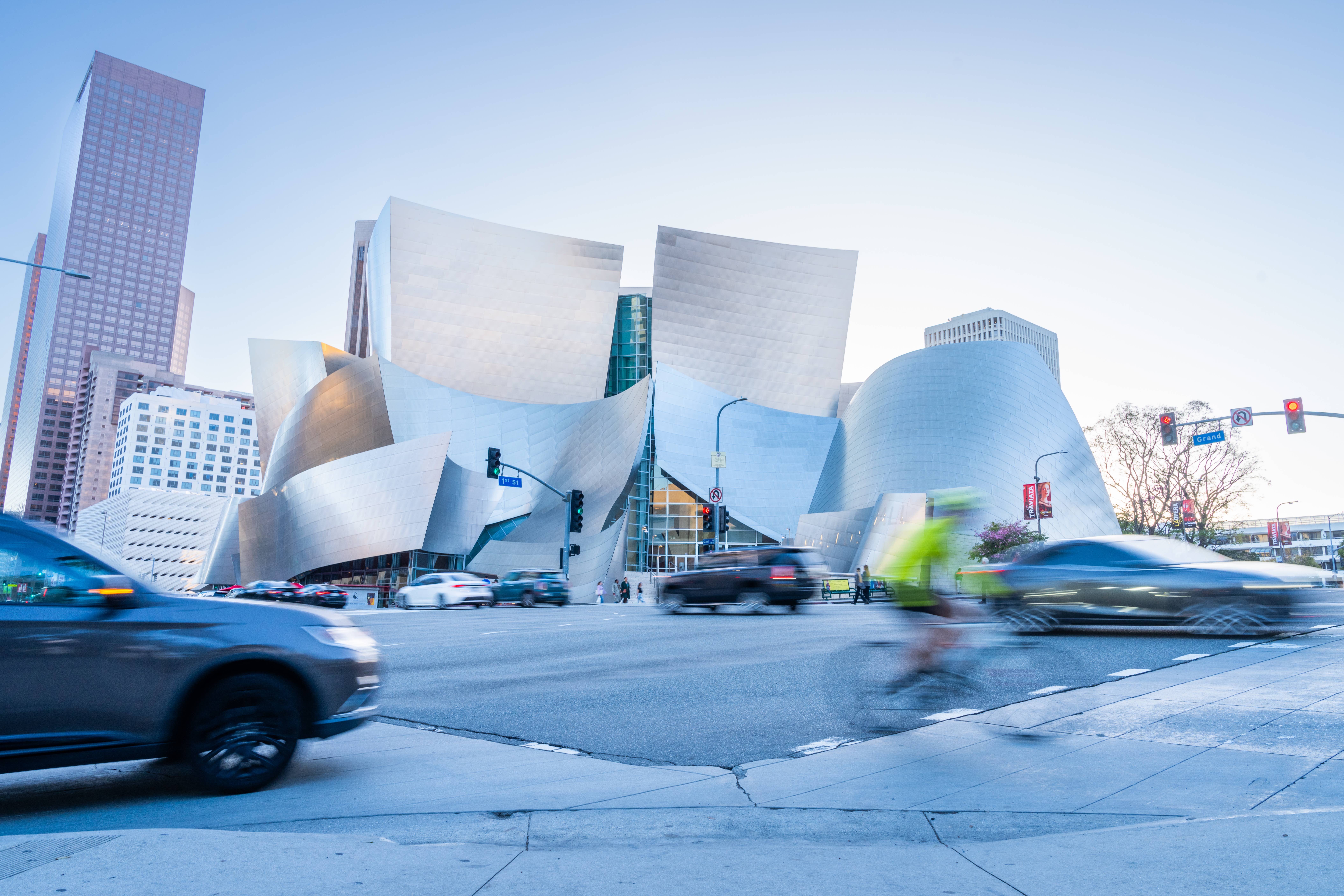 Modern downtown buildings with curved white facade, glass atrium, and traffic blurred by motion at an intersection