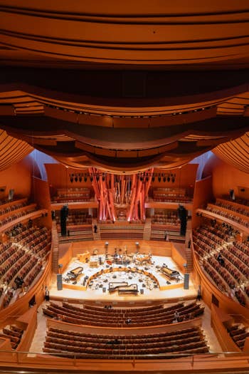 Symphony hall interior with curved balcony seating, stage instruments, and warm orange lighting from above