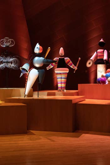 Colorful robot sculptures on a gallery pedestal under warm red lighting in an exhibition room.