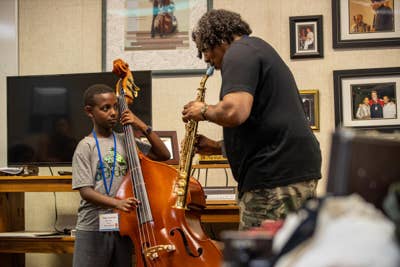 A YOLA student plays a standup bass next to a YOLA instructor playing a brass clarinet. 