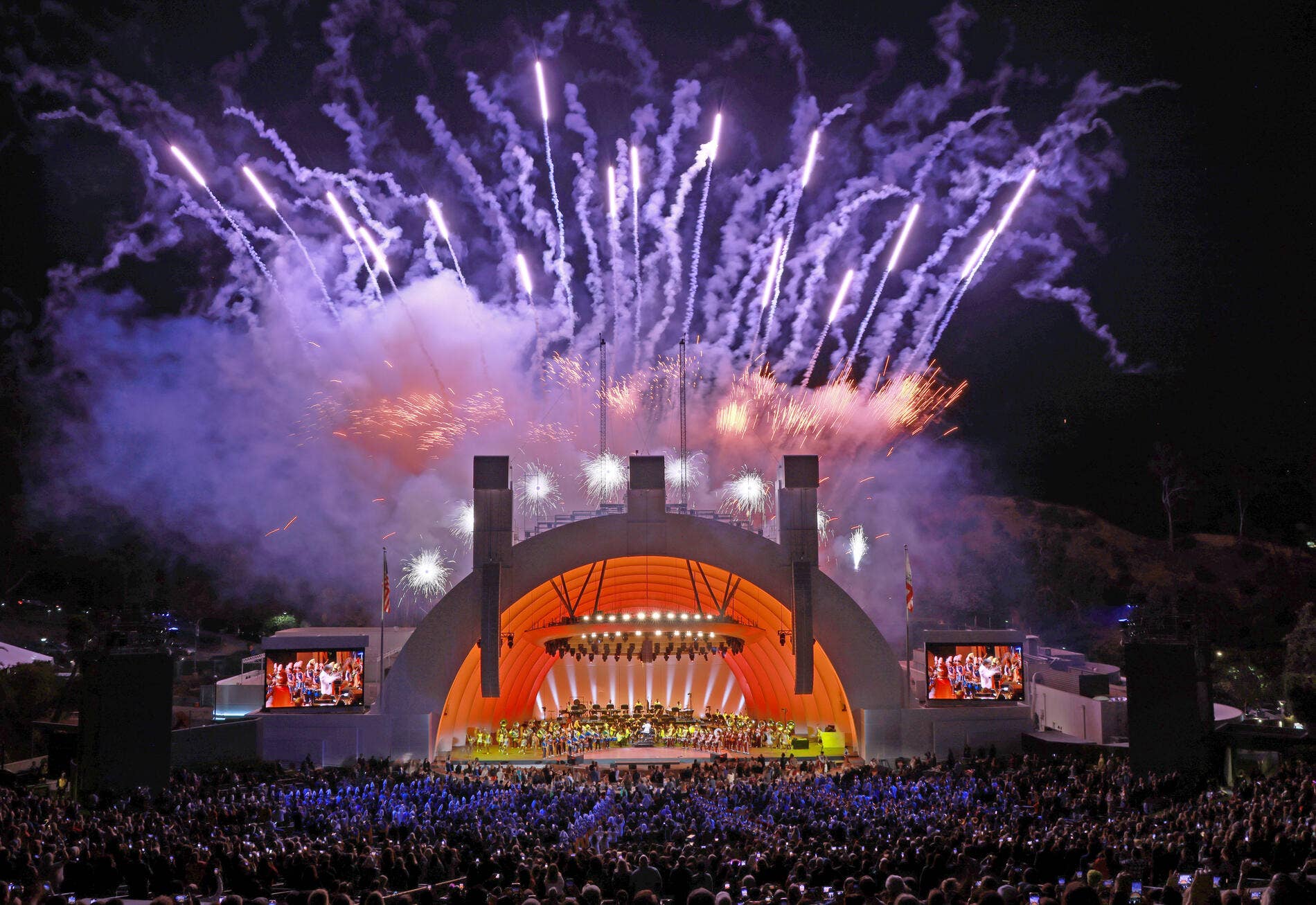 The lit Hollywood Bowl during a performance with fireworks above the stage.