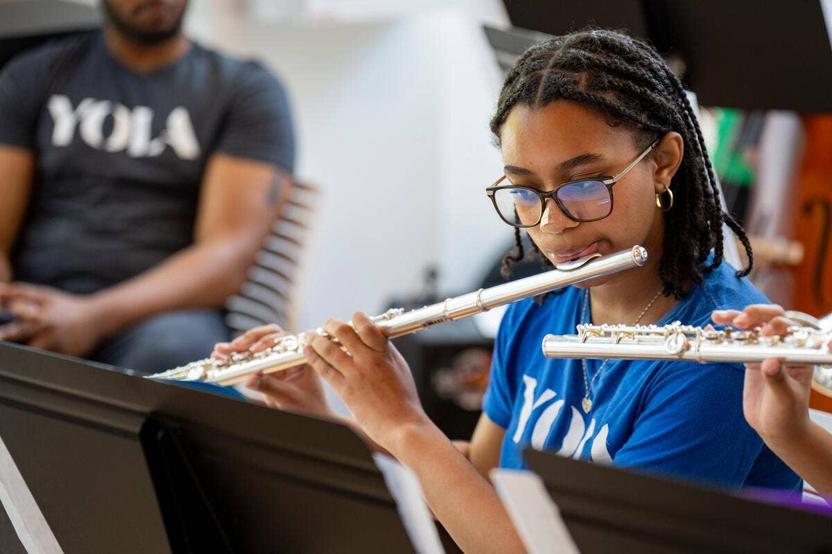 A YOLA student wearing a blue YOLA t-shirt plays the flute.