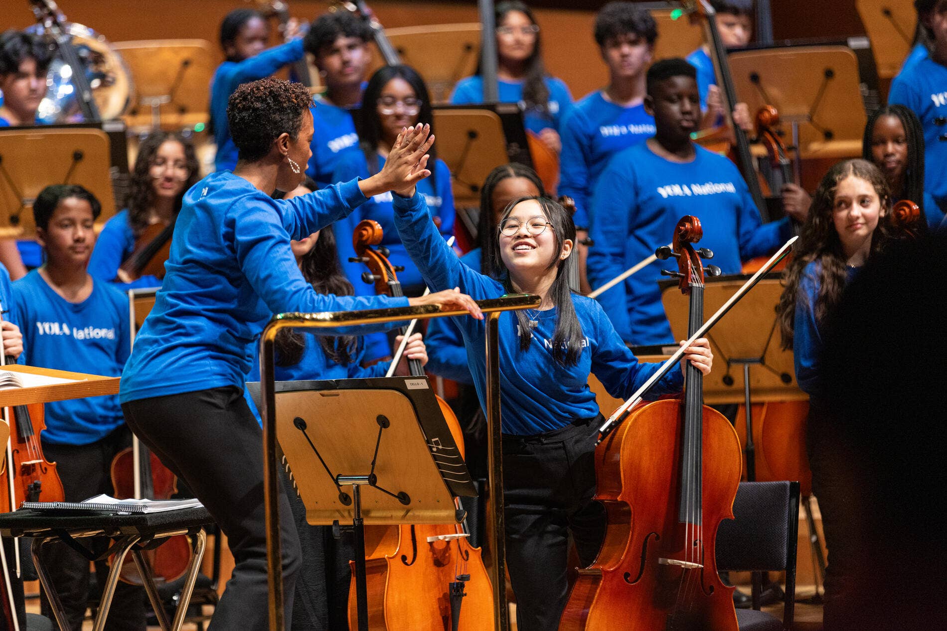 A YOLA National student high-fives the conductor after performing a solo during a performance.