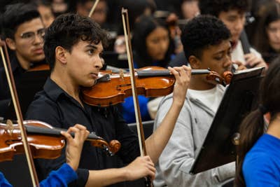 A YOLA student plays the violin among other student musicians during a performance.