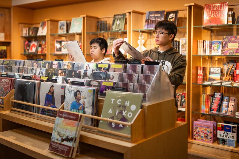 Two students browse vinyl records at a bookstore display with stacks of album covers in the foreground.