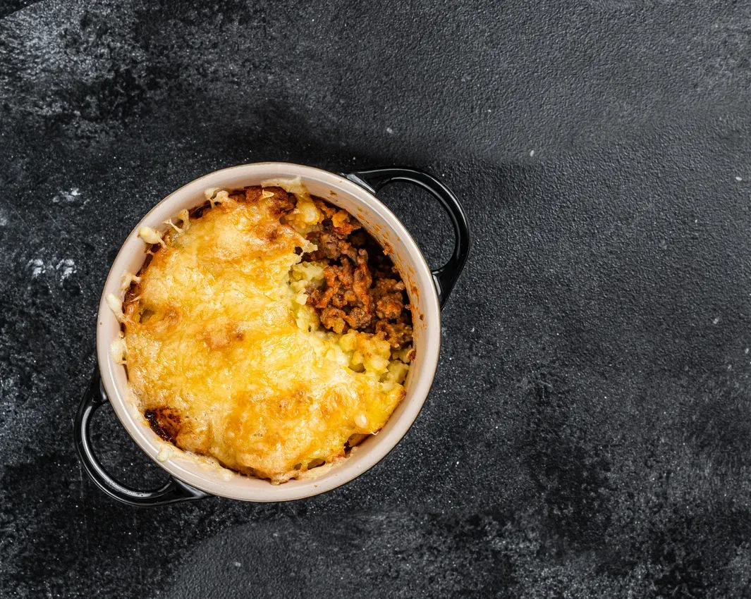 Baked shepherd's pie in a small skillet with a golden, browned cheese crust on a dark countertop.