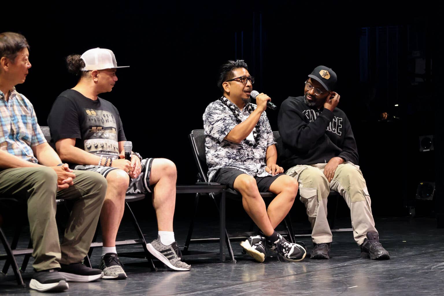 Three men seated on a stage during a panel, one holding a microphone and speaking into it.