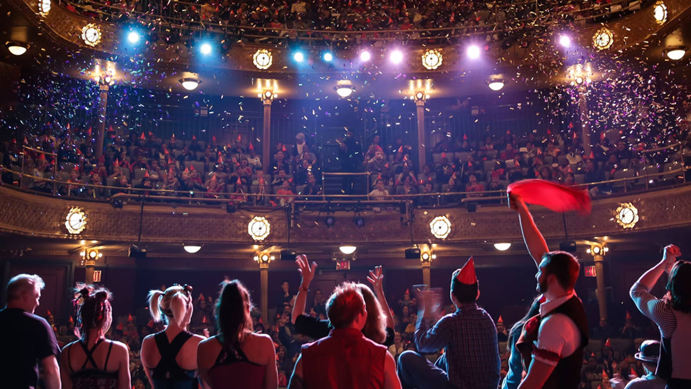 Performers standing in a line on stage face away from the camera toward the audience, and confetti falls.