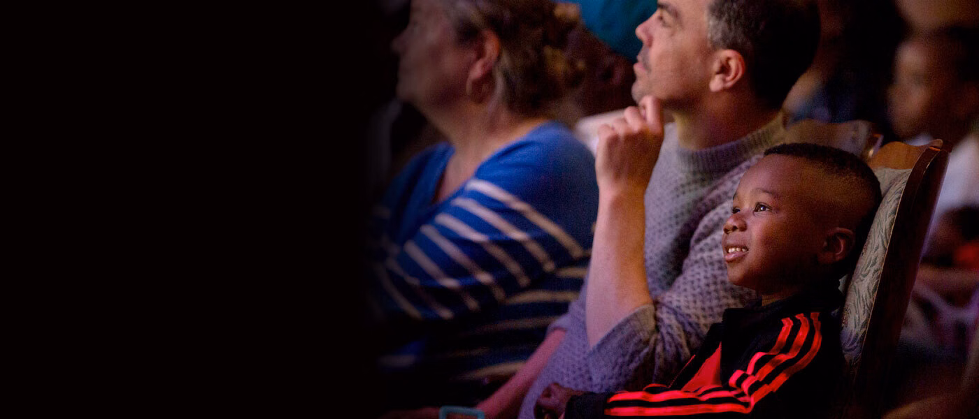 A kid sitting in the audience looks to the left watching a performance.