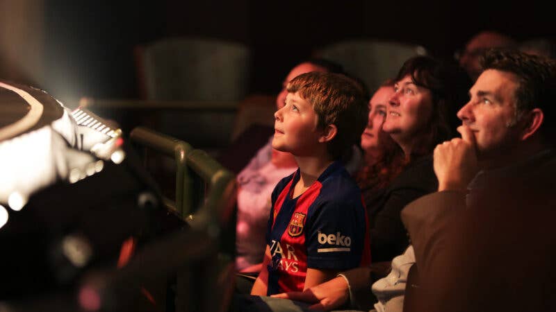 A young boy looking towards the stage from a seat with blurred out seats behind him. 