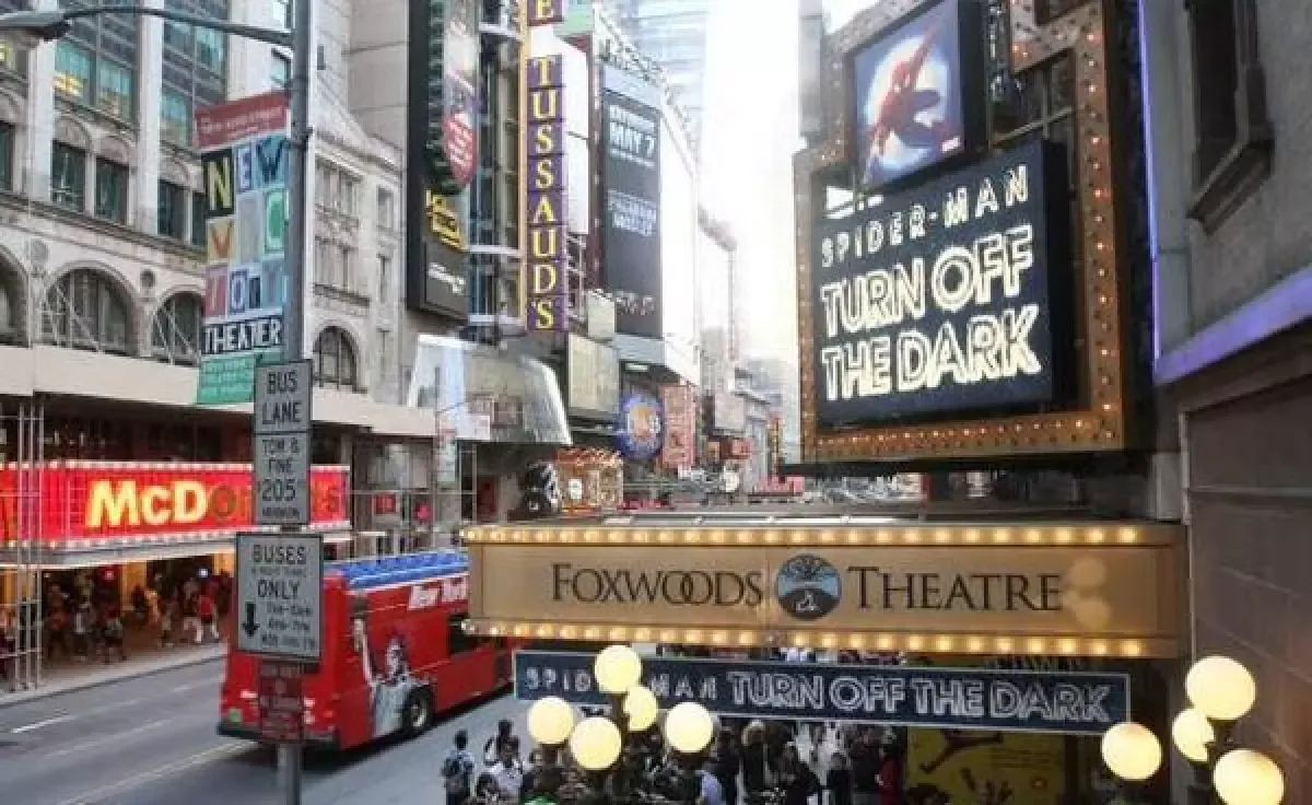 Times Square street scene with billboards and a red bus passing by the Foxwoods Theatre marquee showing Spider-Man: Turn off the Dark.