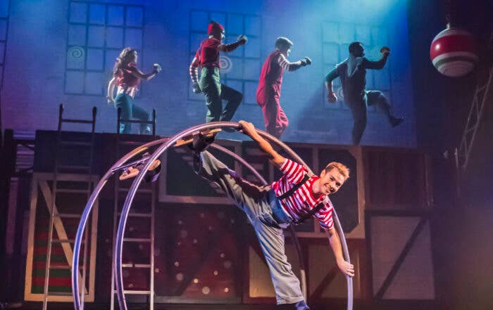 A man wearing a stripped shirt and grey overalls performing with a Cyr wheel.