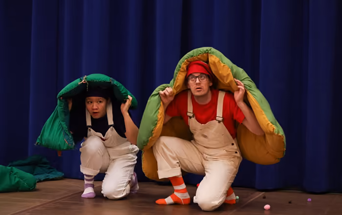 Two performers in overalls with green blankets over their heads 