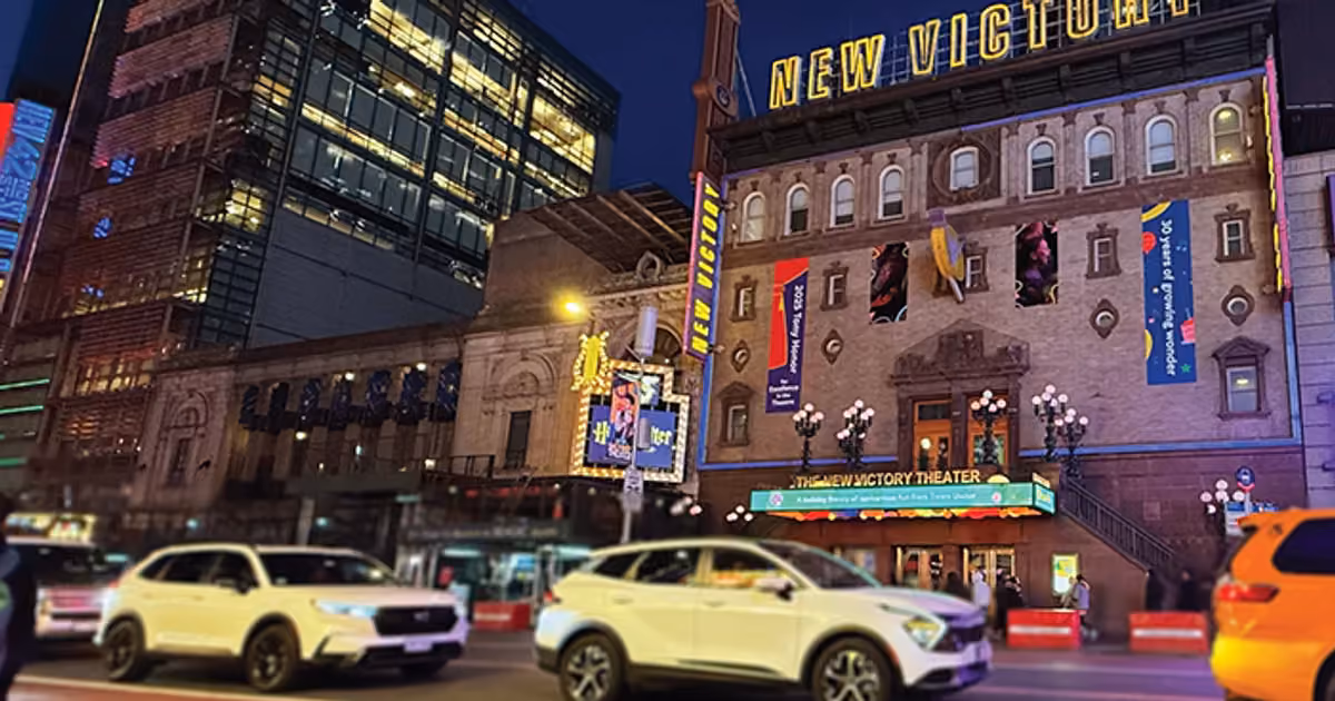 The New Victory facade at night, with cars driving in front