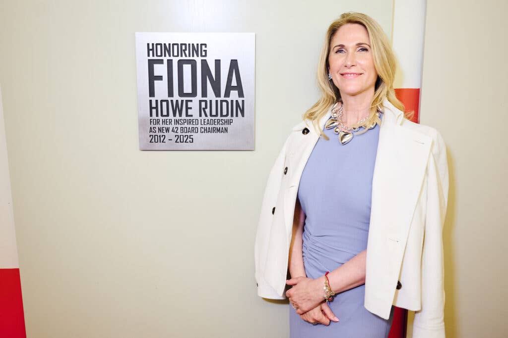 Fiona Rudin in a white blazer and a blue dress standing in front of a sign honoring her leadership.