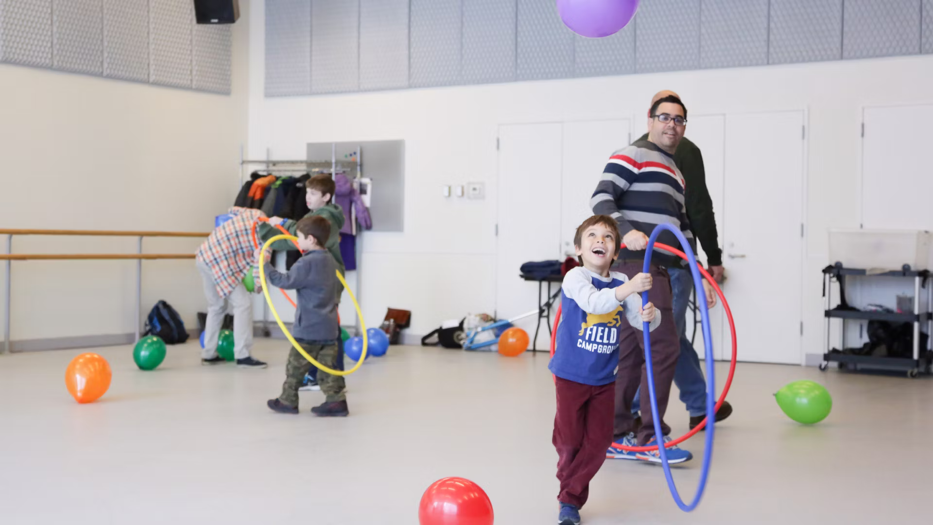 A boy plays with a hula hoop inside a dance studio, as others play behind him.