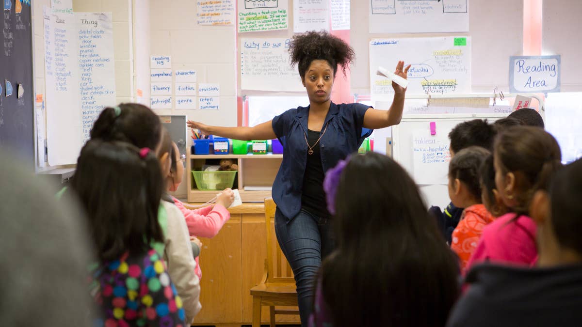 A teacher in a classroom in front of students with her hands out to balance