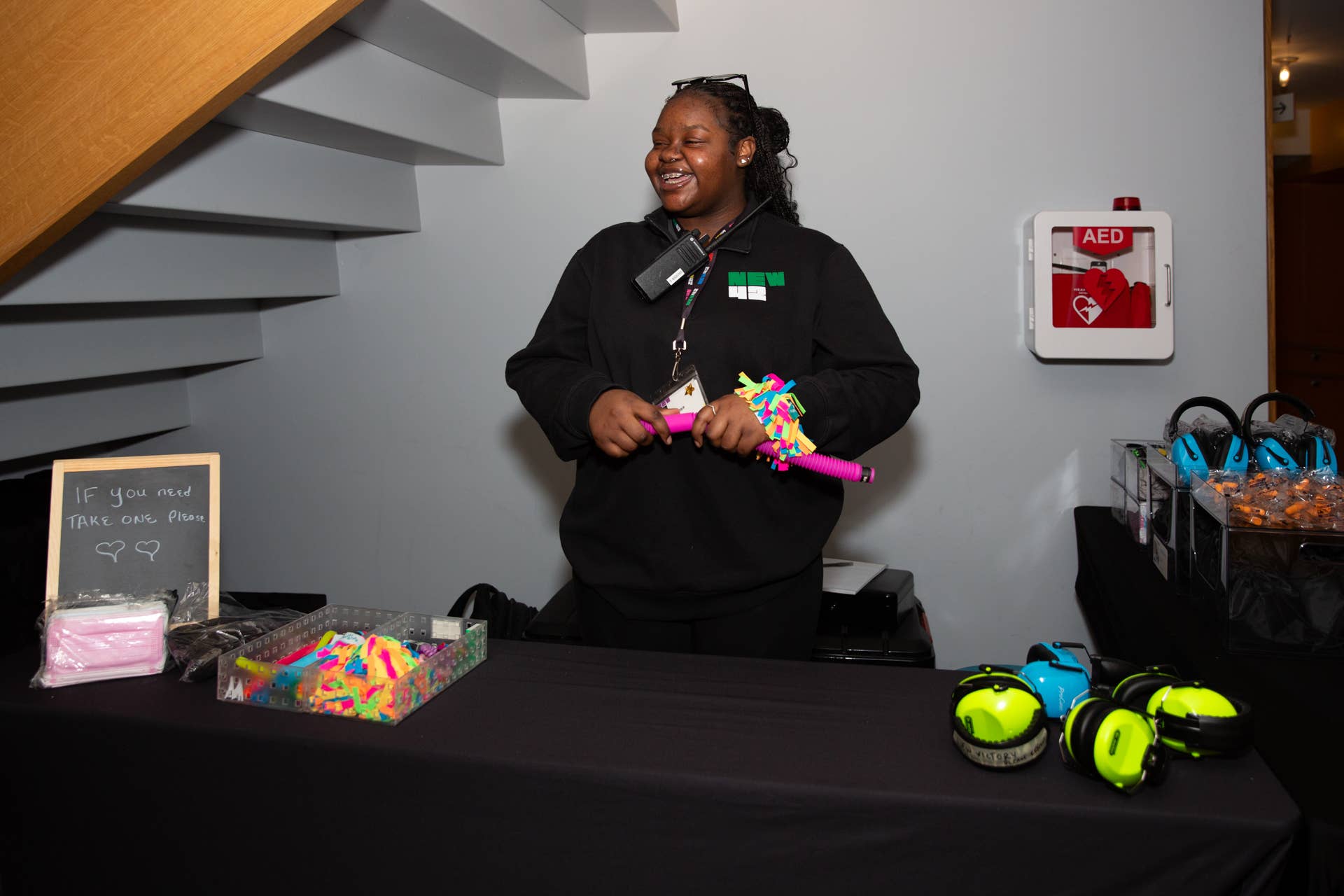 An Usher stands and smiles while holding fidgets at the Accessibility Table.