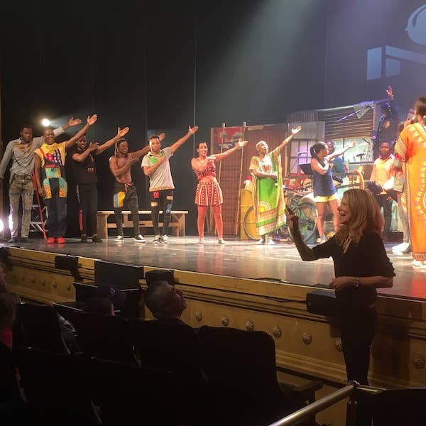 An ASL interpreter signs in front of a stage of dancers and performers during a colorful show