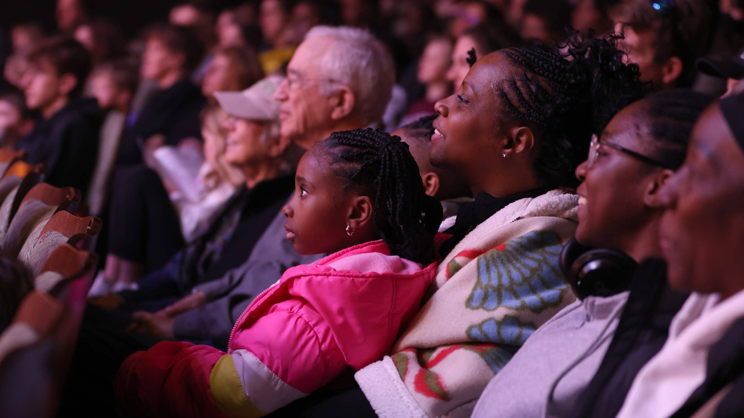 Audience members are seated in the theater, watching with focused expressions