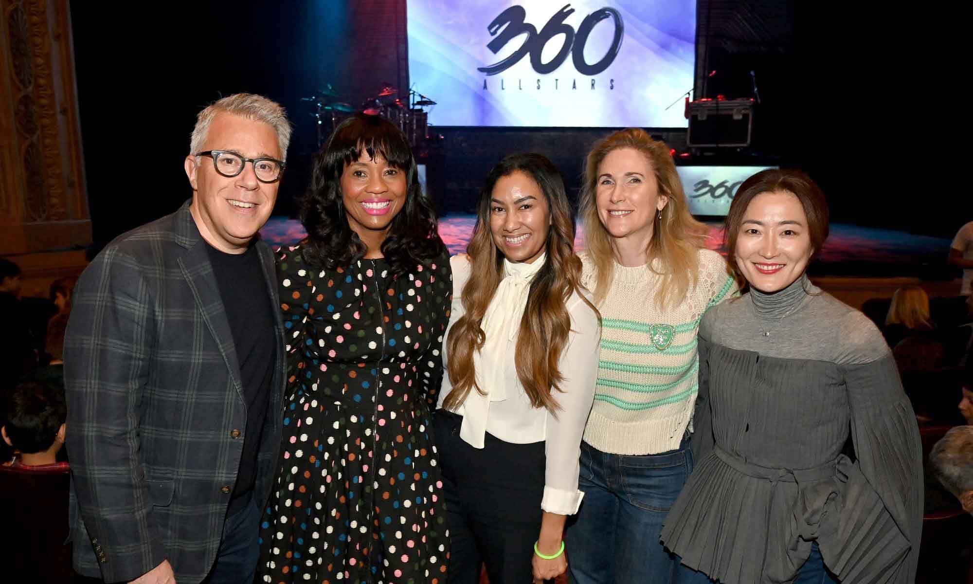 Five people pose together at a 360 Allstars event with a stage backdrop and colorful lights behind them