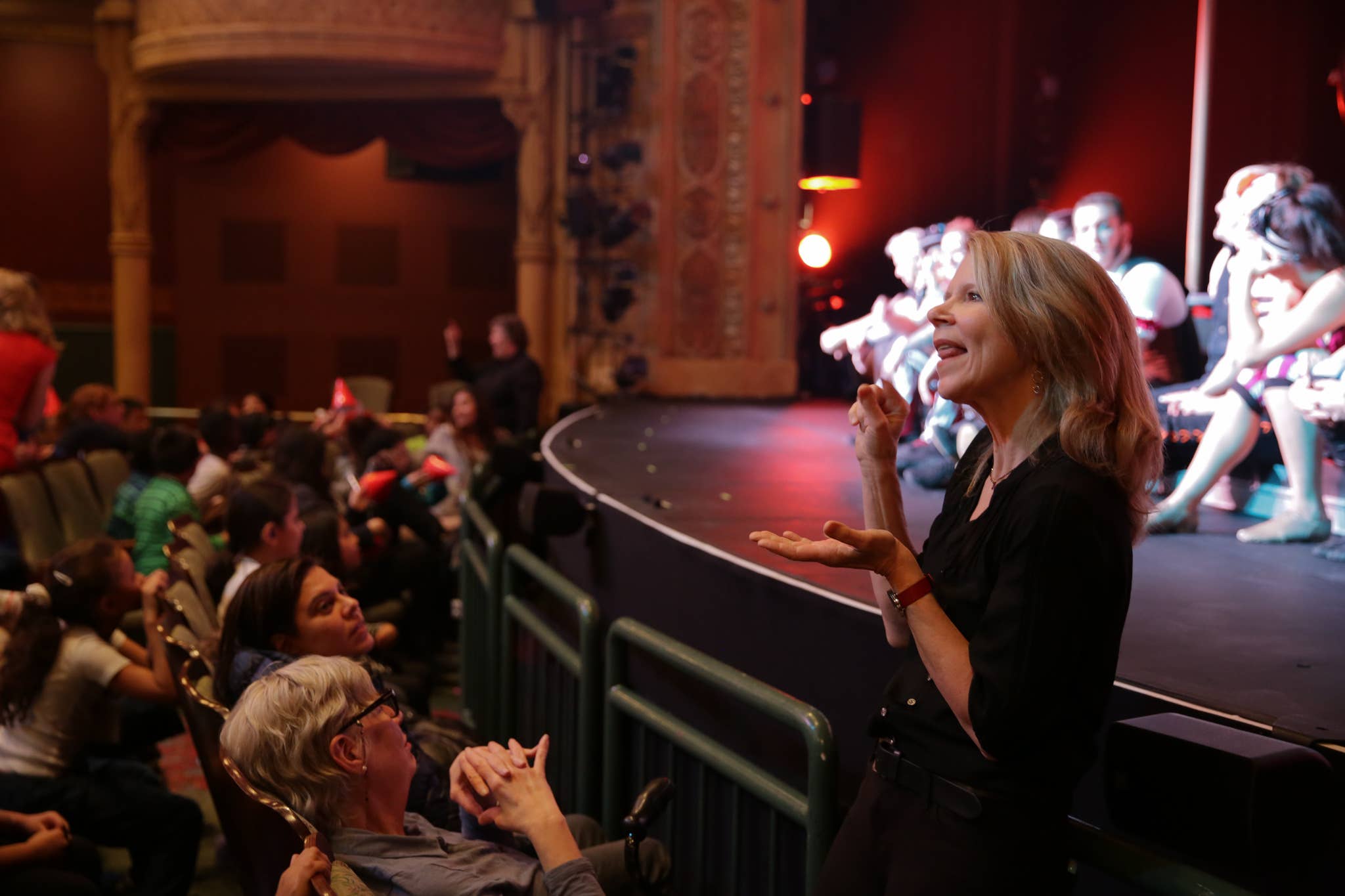 In ASL, a woman interprets the action on stage as the cast of dancers and acrobats acknowledges their band.