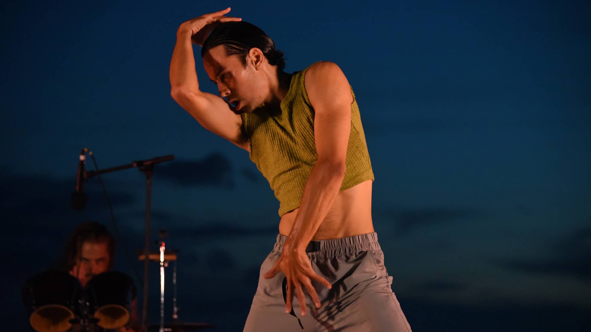 A dancer stands with his arms stretching across his body.