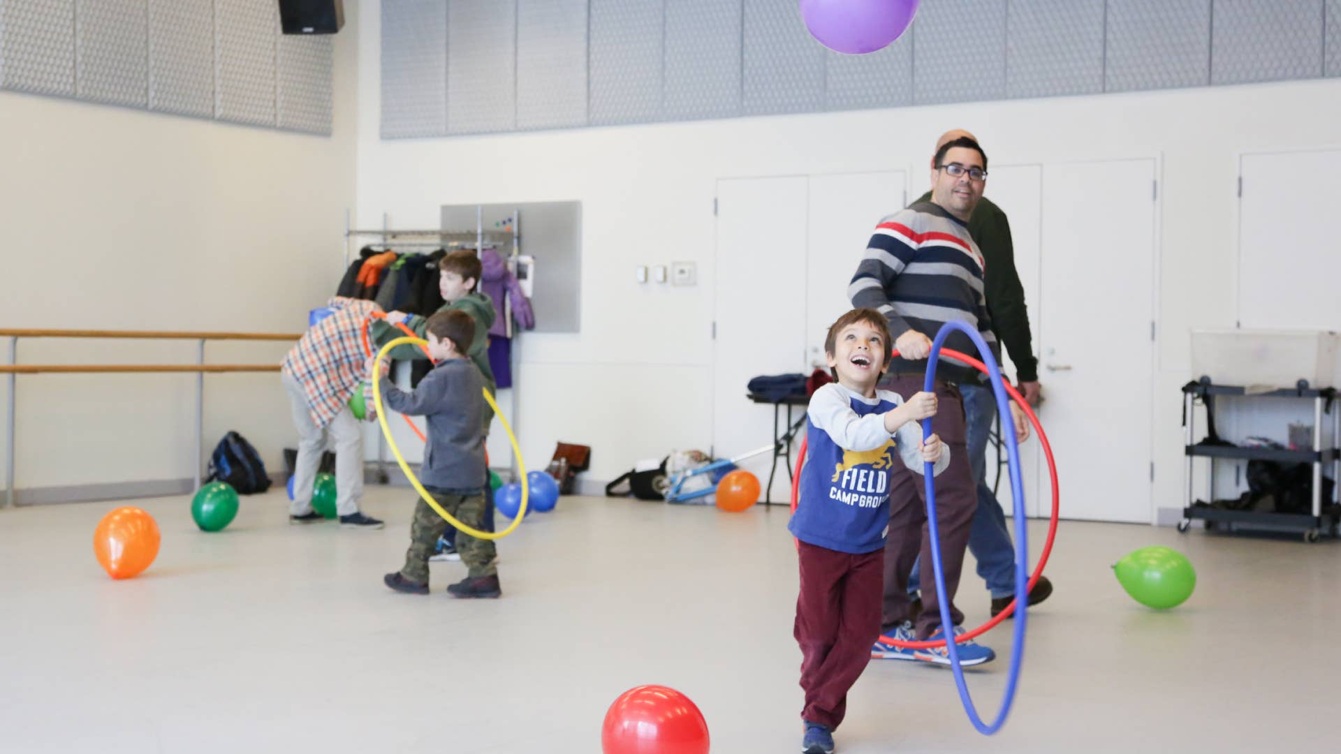 A boy plays with a hula hoop inside a dance studio, as others play behind him.
