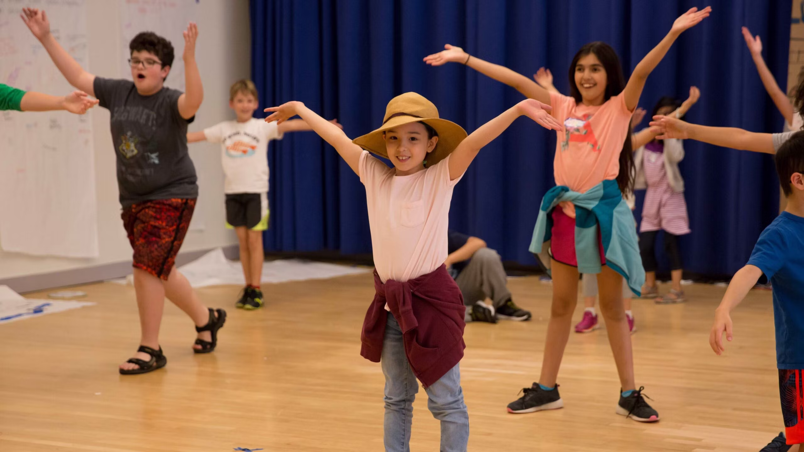 Three kids in the center of a larger group of kids smile at the camera as everyone holds their arms up in air.