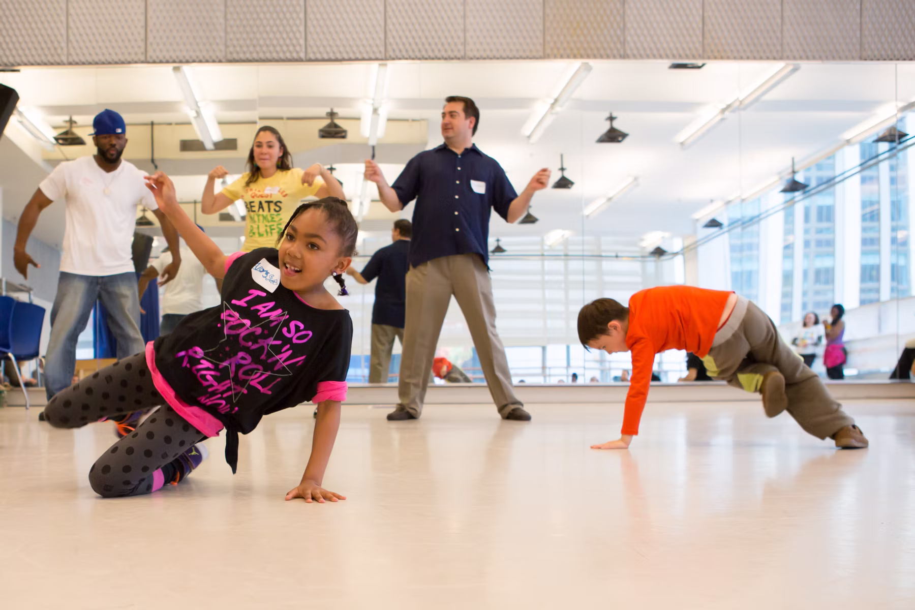 Two kids dance on the ground in front of three adults dancing with their arms up.