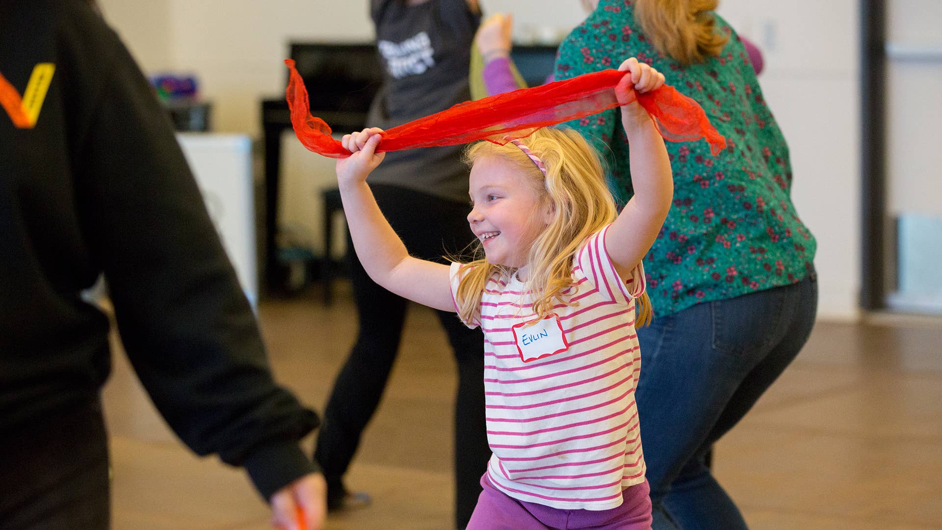 Young girl in pink striped shirt holds a red juggling scarf above her head.