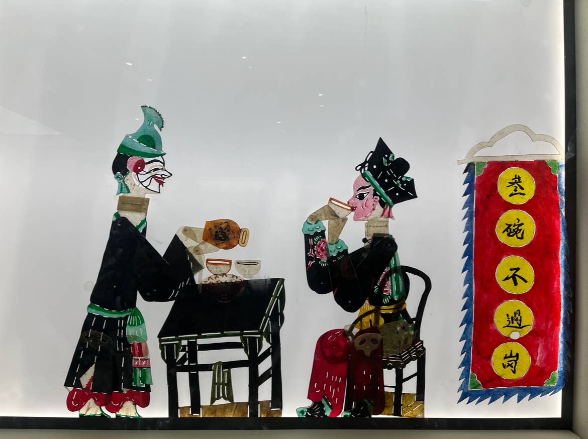 Early chinese shadow puppetry depicting two people sitting for a meal at a table.
