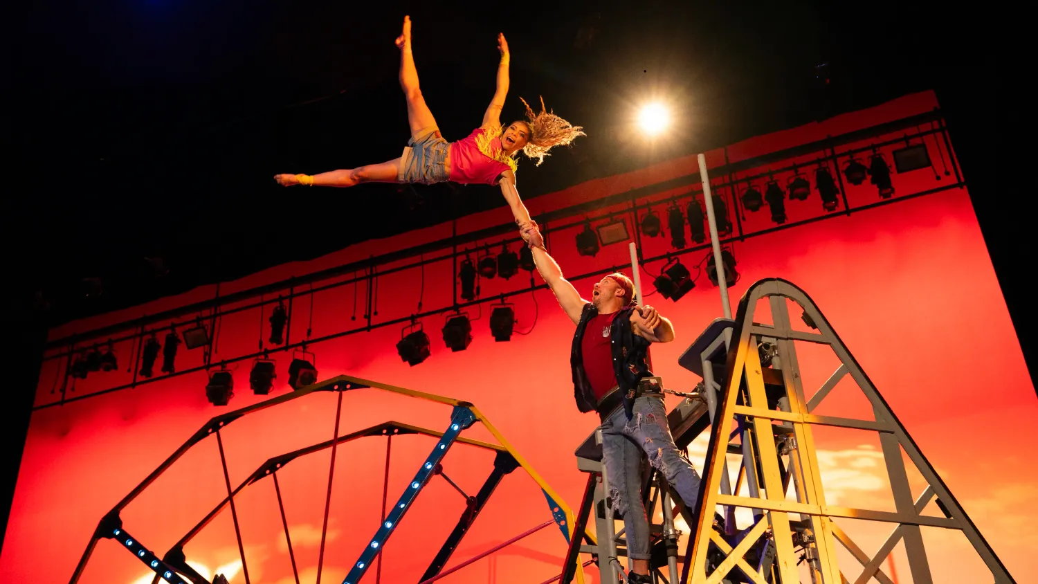 A man stands on top of a roller coaster and swings a woman up in the air, holding her hand.