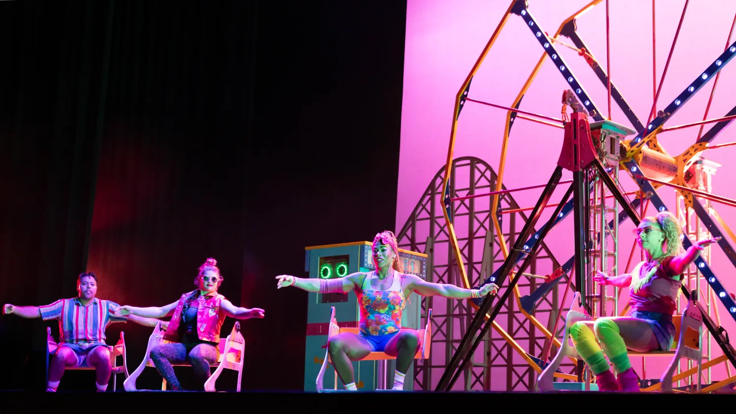 Four performers in bright '80s-inspired clothing sit on benches and hold their arms out to their sides.