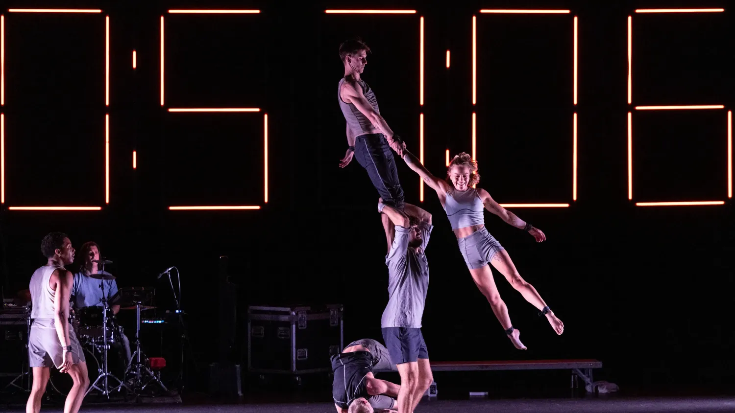 One performer stands on the shoulders of another, holding hands with a third performer, who is held in the air.