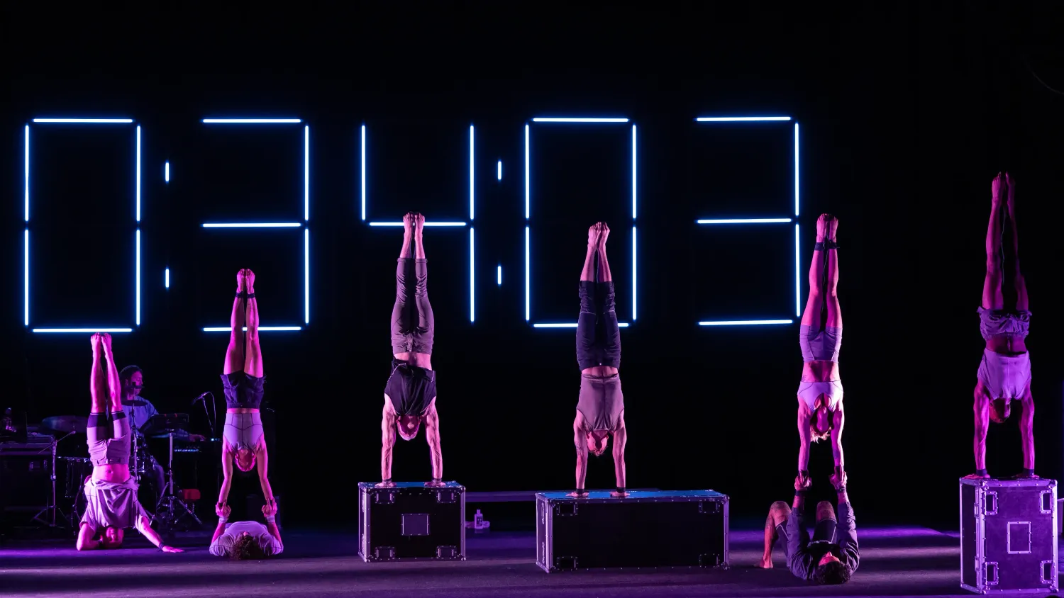 A performer headstands, two performers handstand on a partner's hands and three performers handstand on boxes.