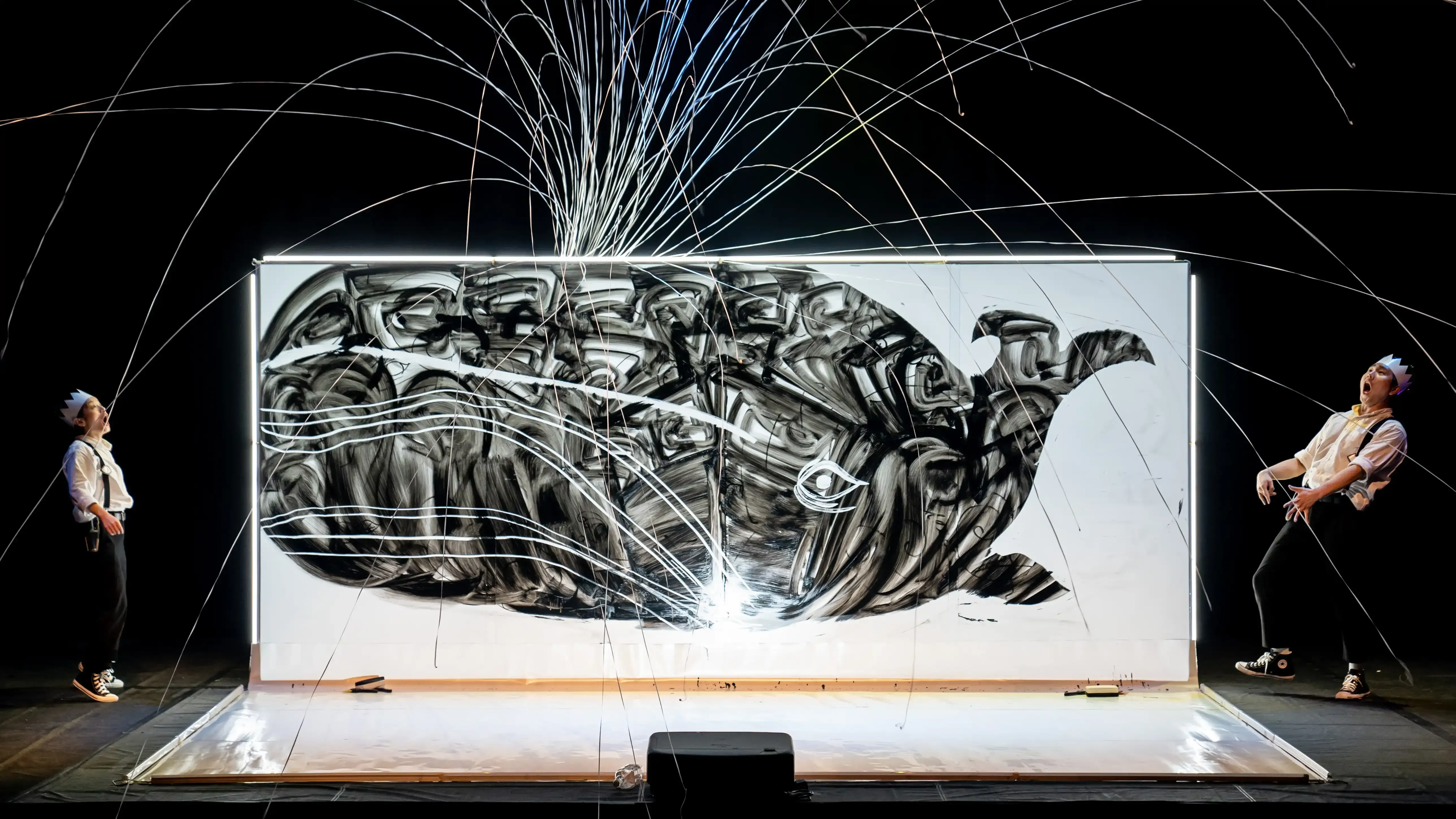 A pop of confetti shoots out of the blowhole of a large whale illustration. Two performers watch with awe.