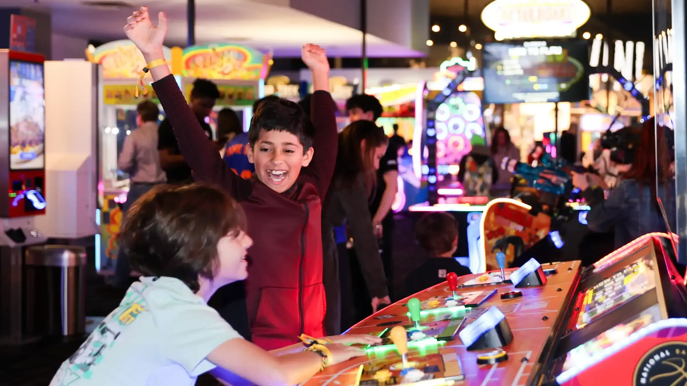 Two kids play a game at Dave & Buster's. One kid smiles and lift his arms in the air.