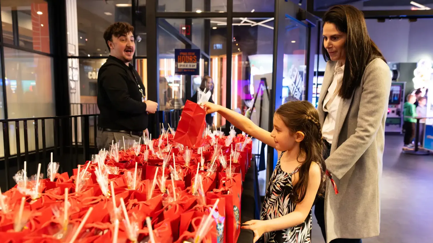 A kid and parent pick a red gift bag from a table full of gift bags.