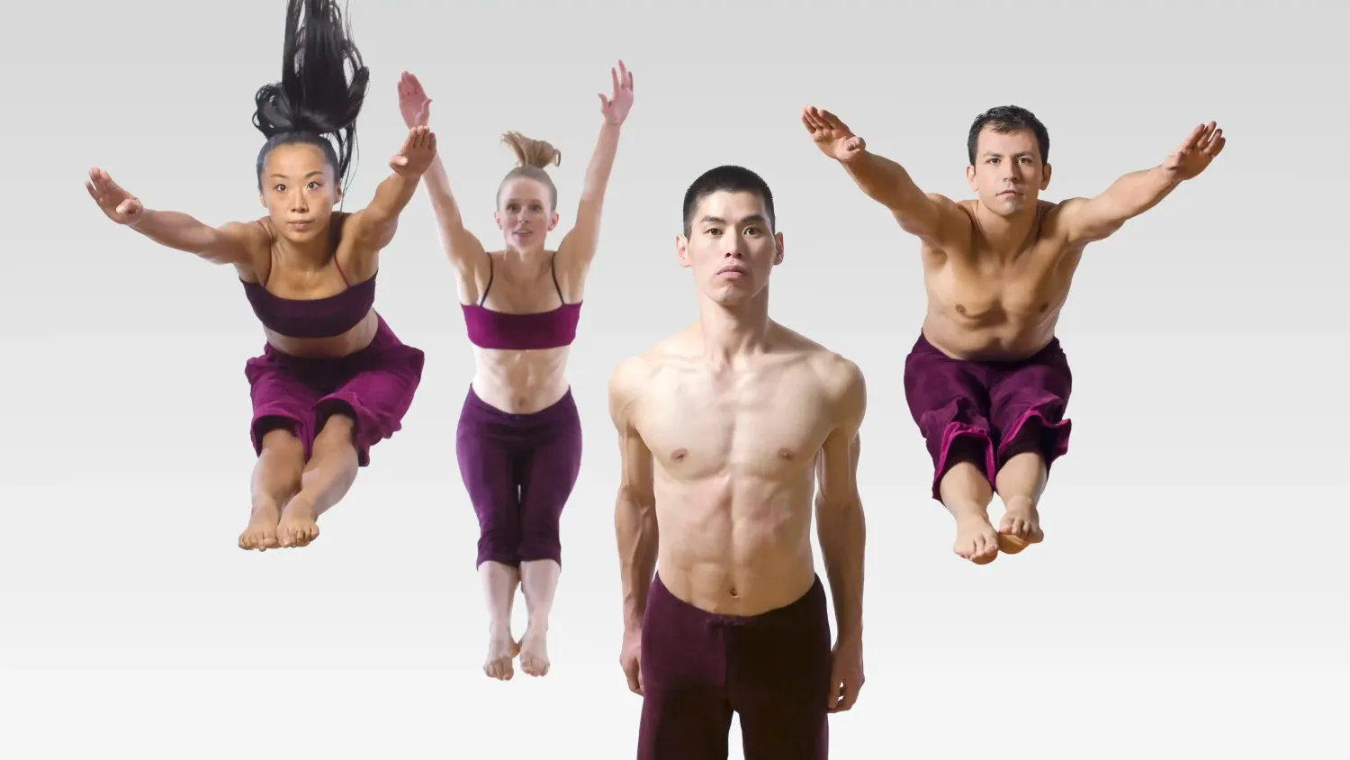 Three dancers in violet clothing jump with their arms and legs extended forward. Another dancer in violet pants stands with his arms at his sides and looks straight ahead.