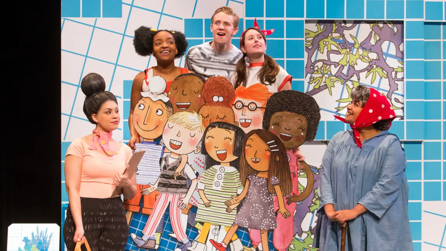 A group of three real and eight cardboard students stand clumped together. A woman on the left holds a clipboard. A woman on the right holds a cane and wears a red headscarf with white polka dots.