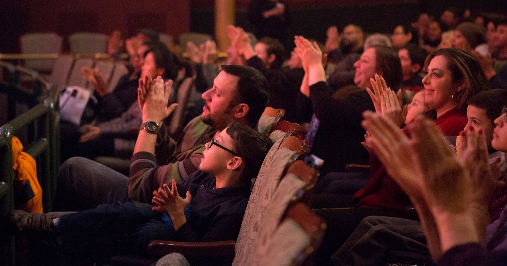 Audience members clap in a dim theater