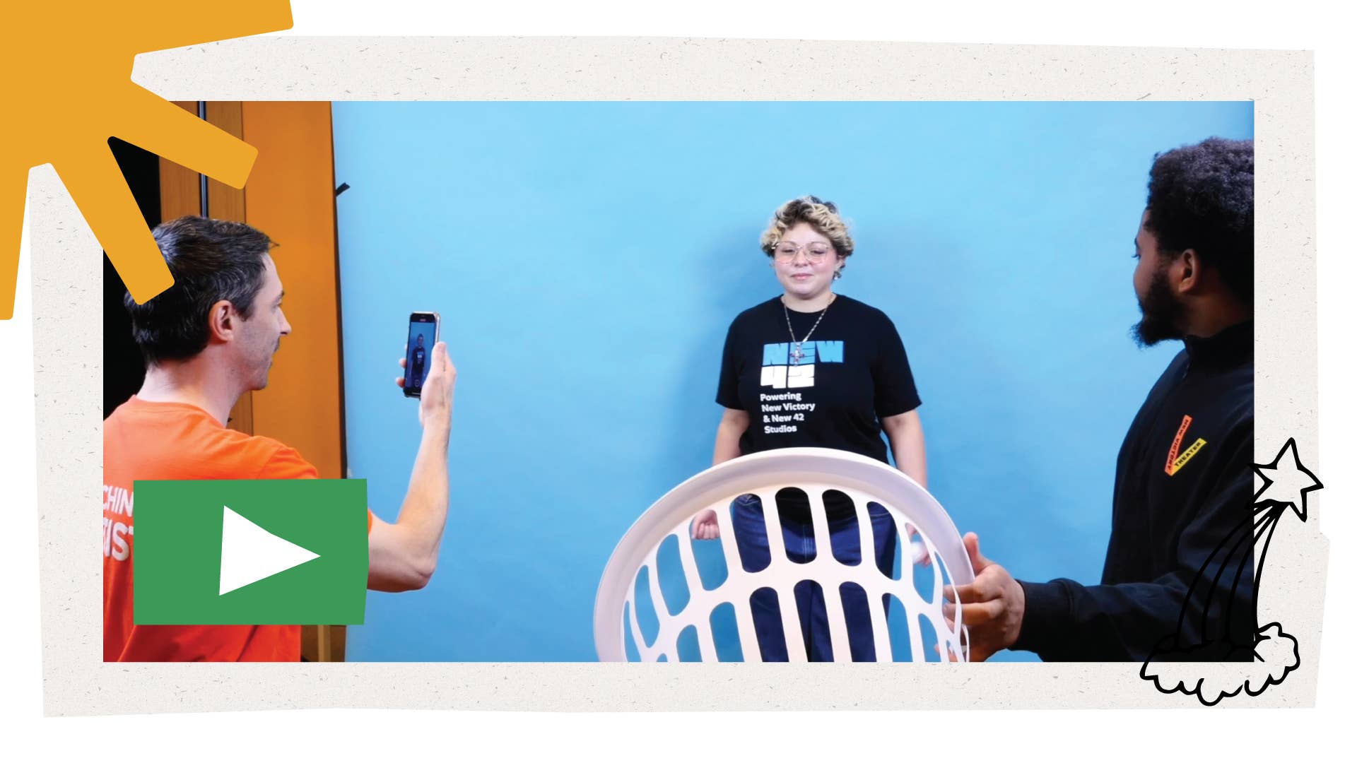 A New Victory Teaching Artist films two Youth Corps members on his phone, and one of them holds up a laundry basket. In the bottom left is a green play button.