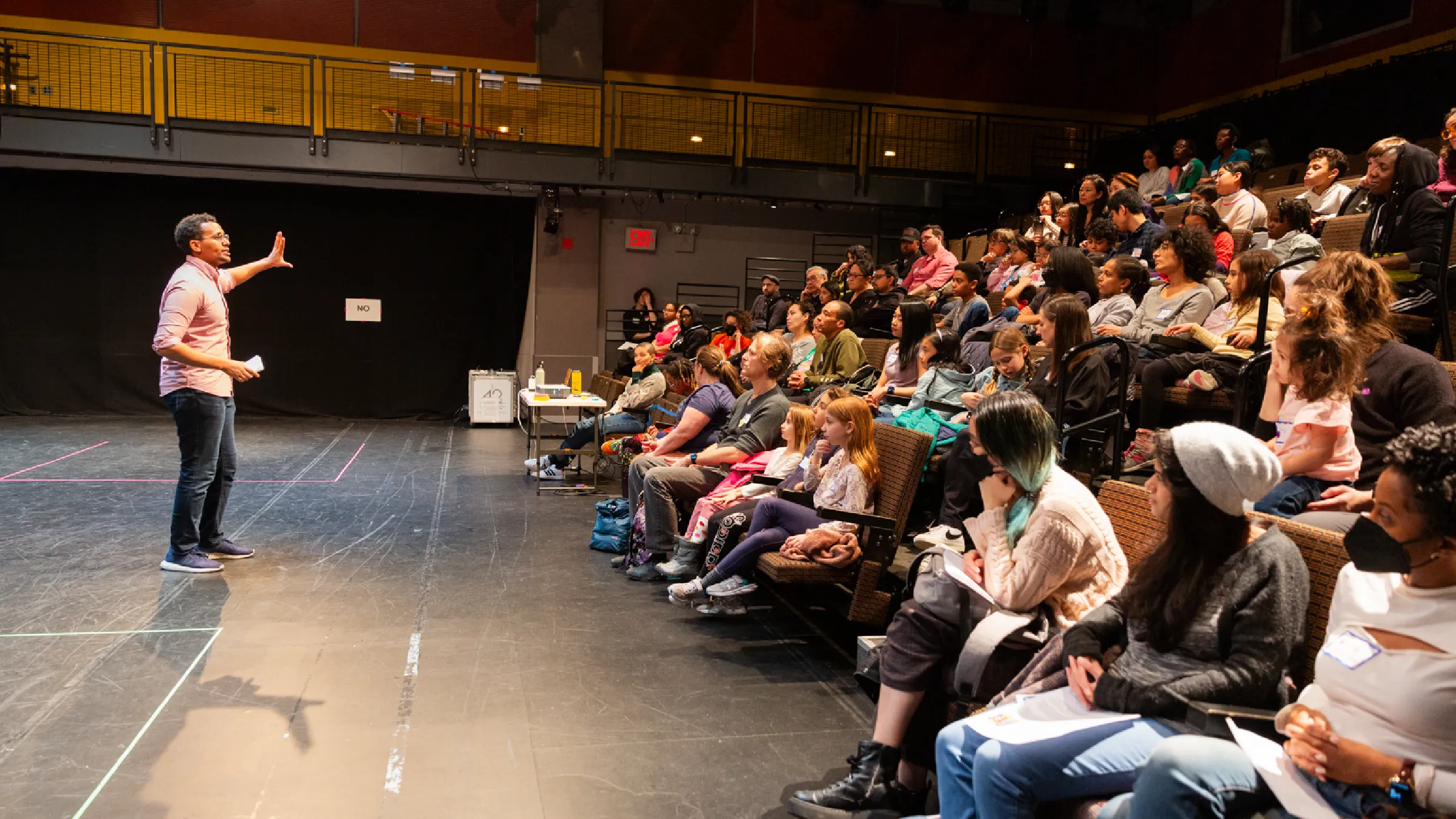 Instructor gestures while addressing a seated group of artists in a school auditorium.