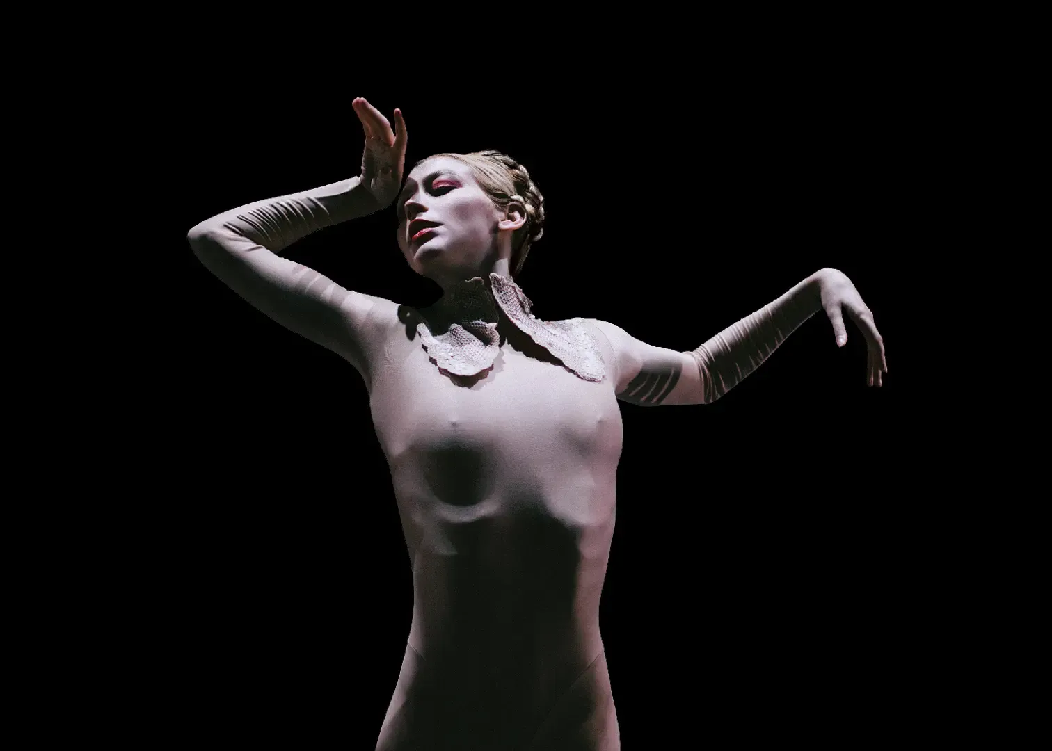 Dancer in a white body suit performs with arms raised against a dark background, head tilted upward.