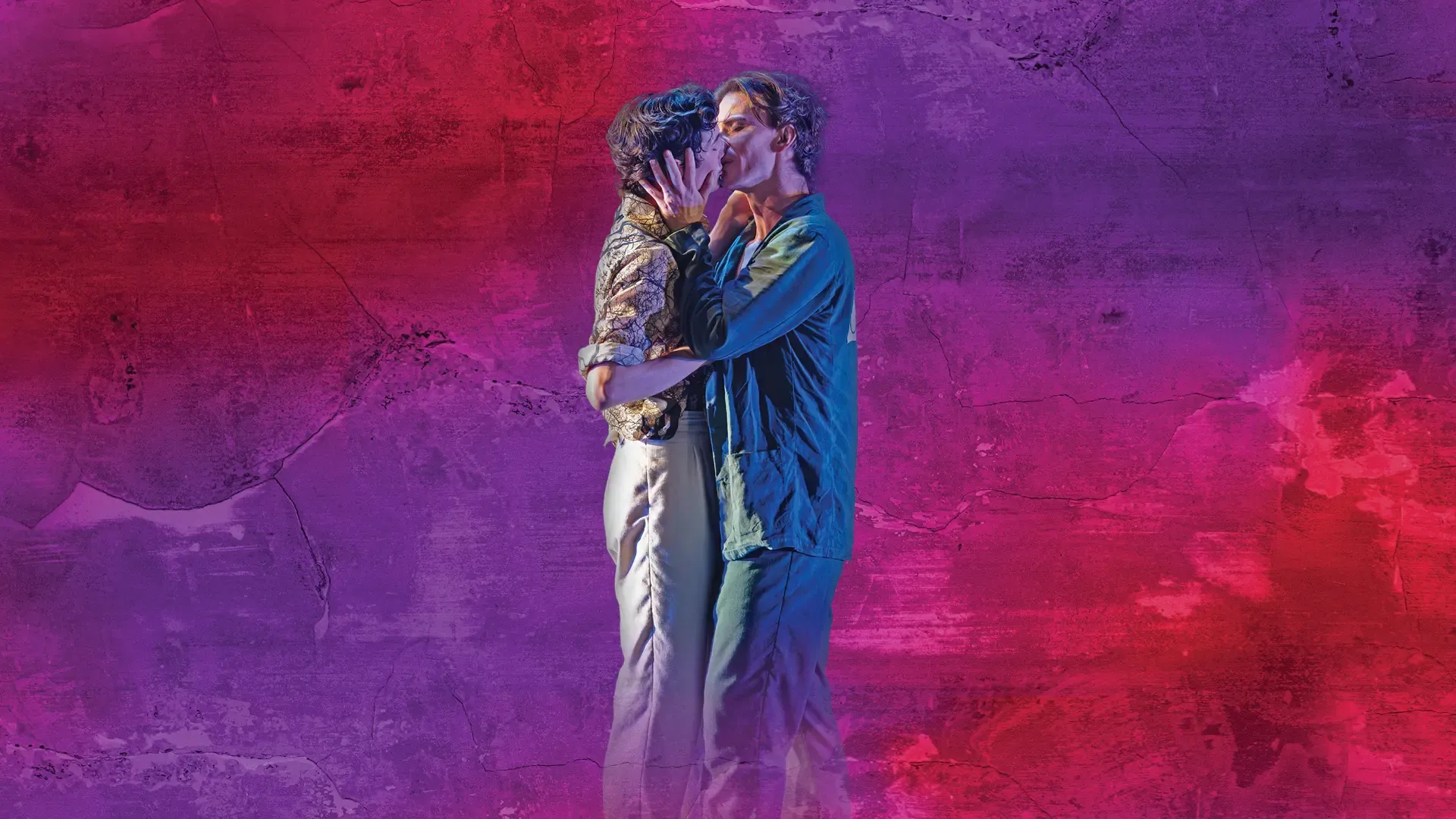 Two men dance and embrace, kissing and smiling against a textured purple and pink wall background.