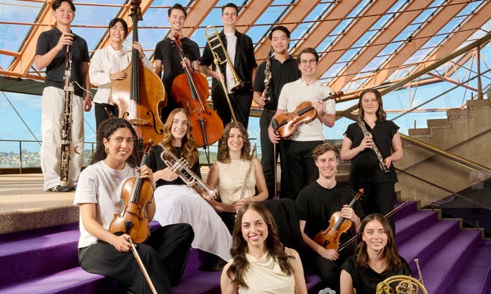 Group of musicians with various instruments pose on purple steps in the Sydney Opera House Northern Foyer.